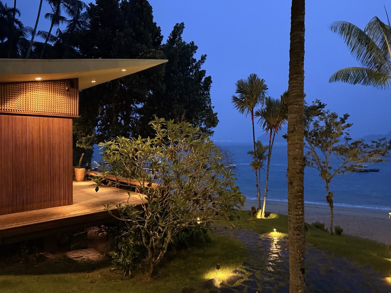 Bangalô de madeira em balanço sobre o deck à beira-mar, voltado para a enseada e a praia ao crepúsculo
