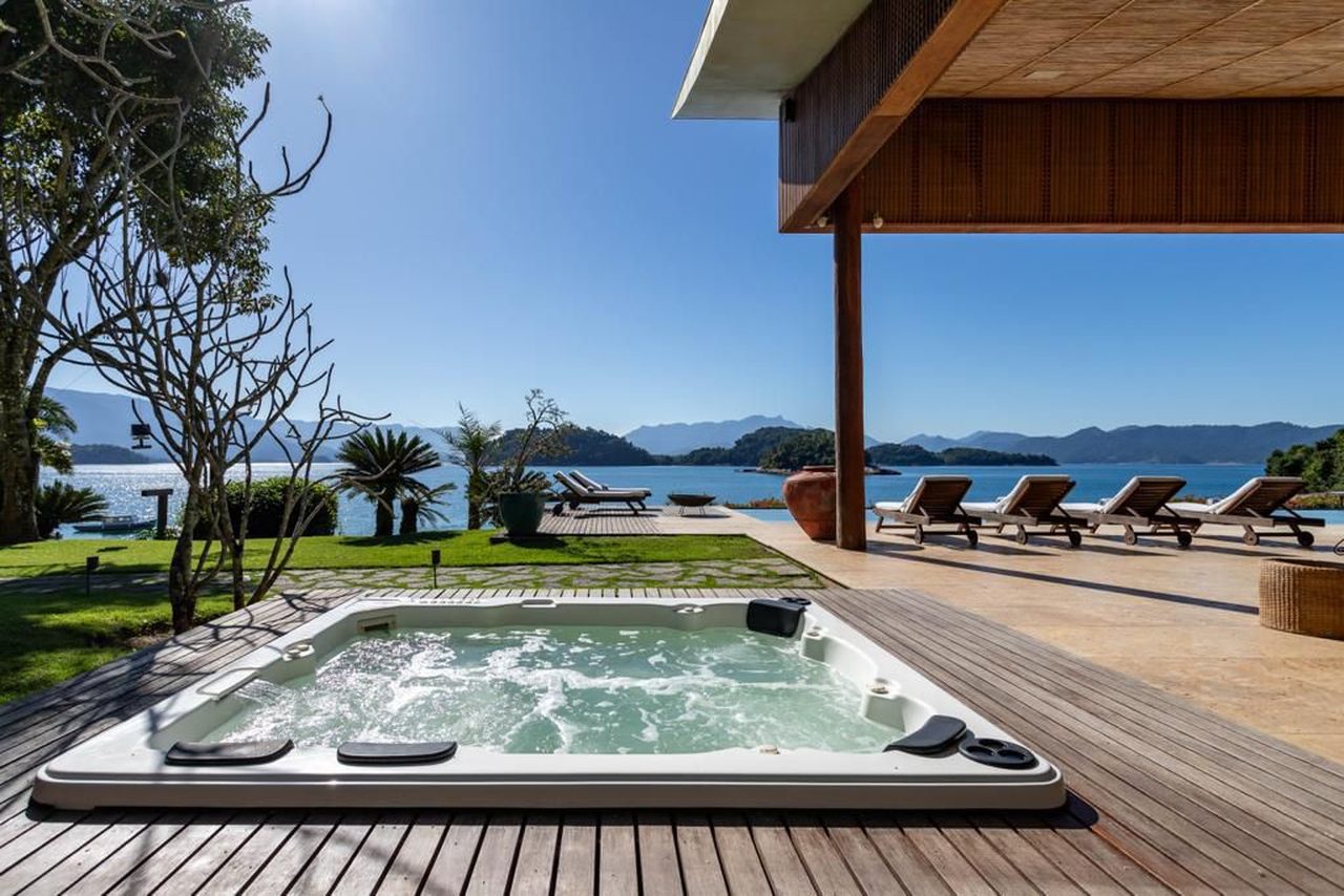 Jacuzzi embutida no deck de madeira, com espreguiçadeiras voltadas para o mar da enseada e as ilhas