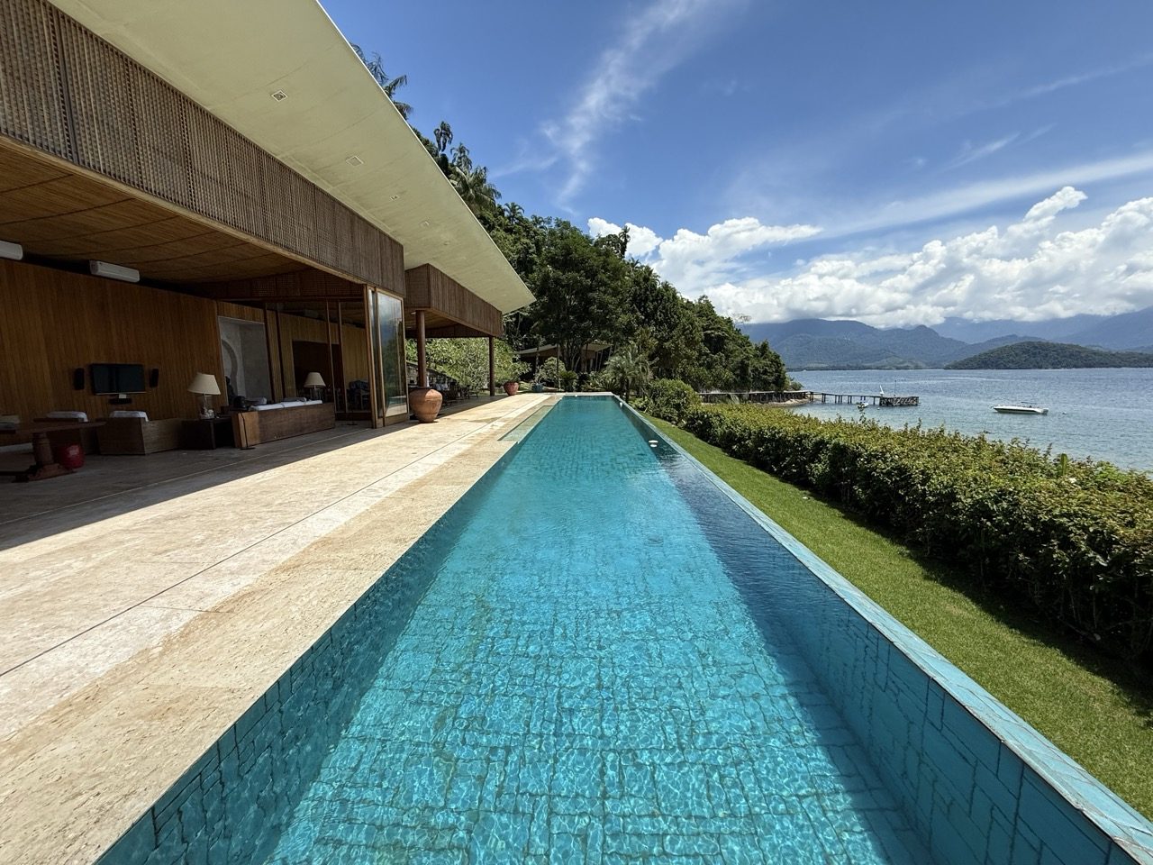 O estar abre-se sob amplo beiral de madeira para a piscina de borda infinita e o mar