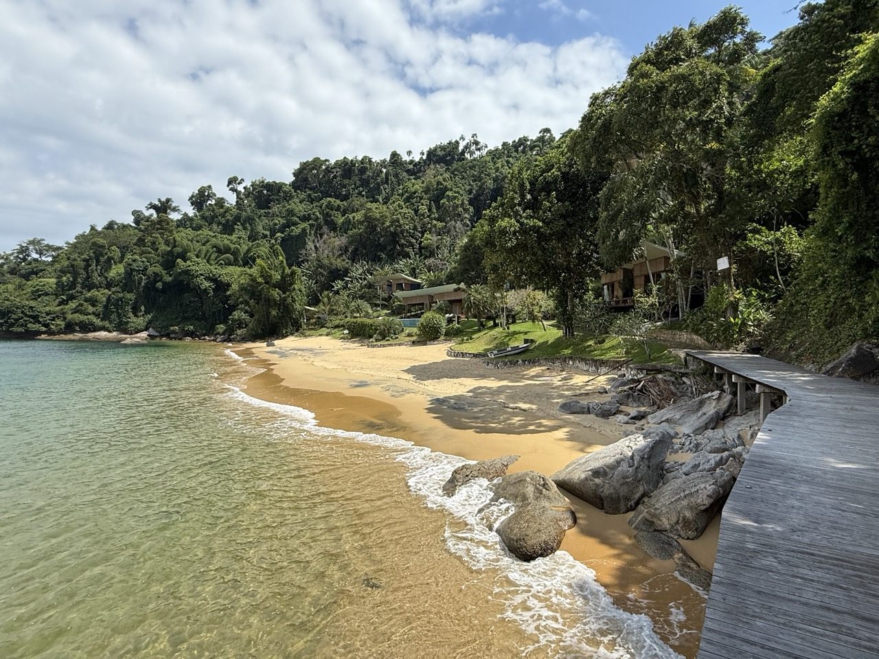O passadiço de madeira sobre as pedras conduz à praia privativa, que desenha uma curva de areia até a casa na mata