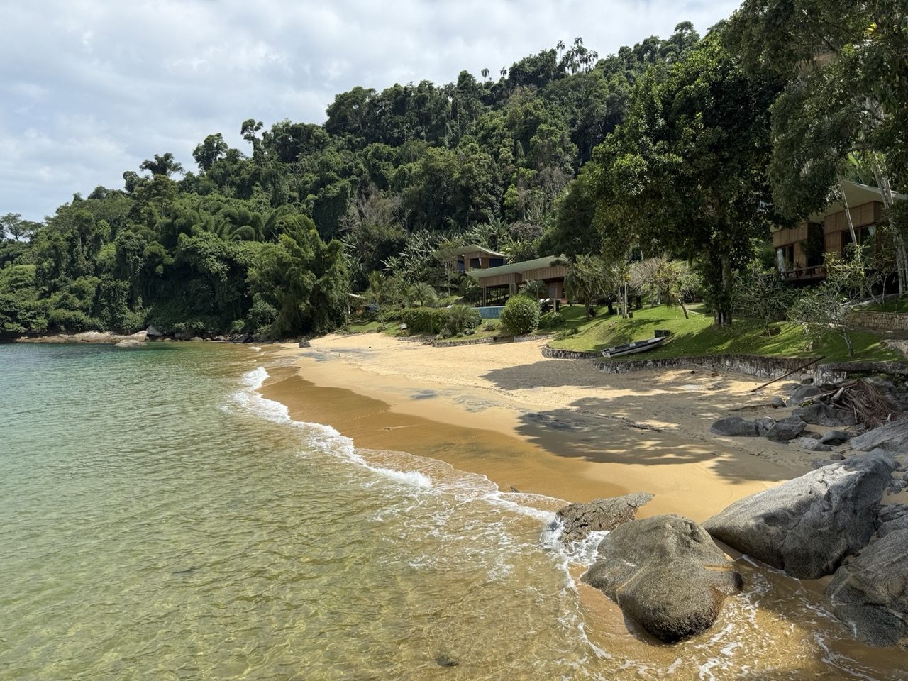 A praia privativa em meia-lua dentro da enseada, com a residência recolhida na mata atlântica e as águas calmas e cristalinas em primeiro plano